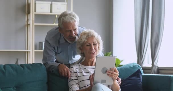 Smiling old couple talking using tablet computer at home - Felvétel, videó