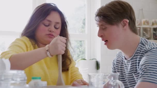 Young Downs Syndrome couple in kitchen at home mixing ingredients in bowl by hand for cake recipe together - shot in slow motion - Metraje, vídeo