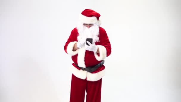 Santa Claus on a white background with a black phone writes SMS and talks on it. - Záběry, video