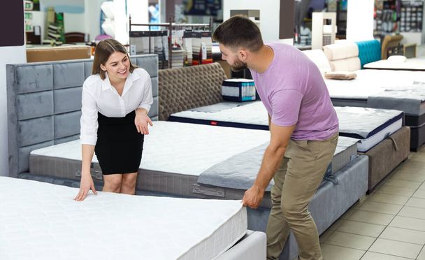 Young saleswoman helping customer to choose new modern orthopedic mattress in store - Photo, Image