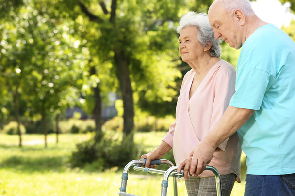 Anciano ayudando a su esposa con el marco de caminar al aire libre
 - Foto, Imagen