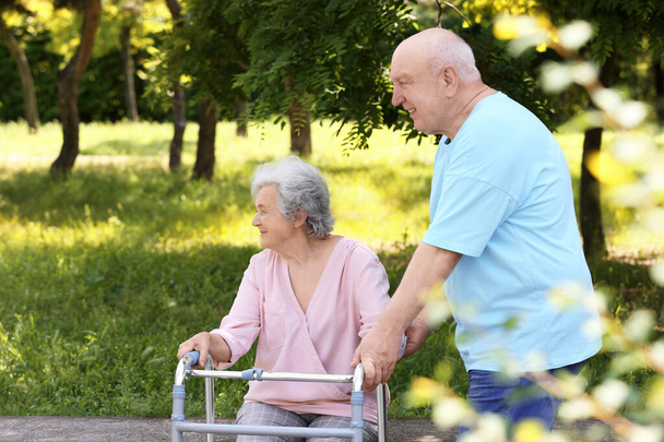 Elderly man helping his wife with walking frame outdoors - Foto, Imagen