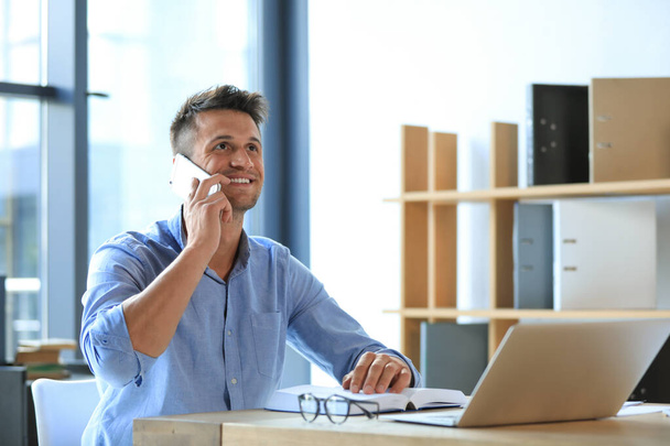Male business trainer talking on phone while working with laptop in office - Foto, imagen