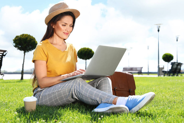 Beautiful woman with laptop sitting on green lawn outdoors - Foto, afbeelding