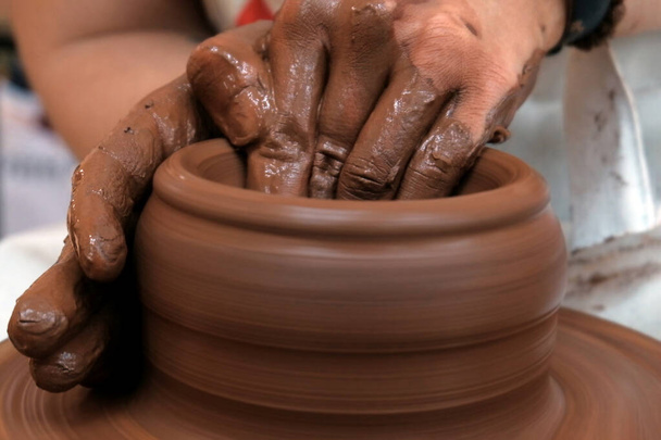 女性または男性の手は回転する陶器の車輪の上にボウルを形成します。赤い粘土で作業します。伝統的な手作り料理。フィールドの浅い深さ。選択的フォーカス。スペースのコピー. - 写真・画像
