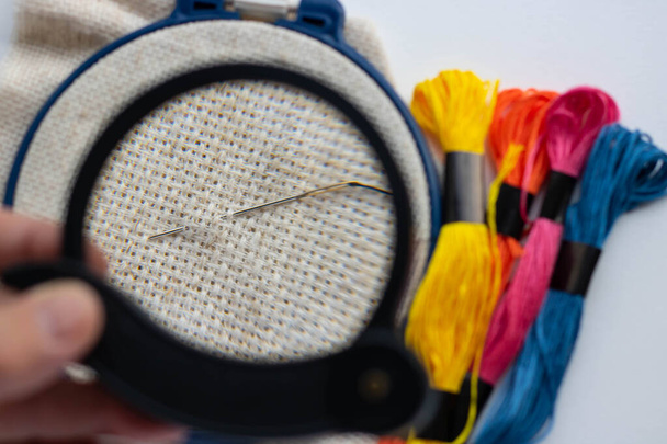 Grandma's hobby, embroidering. Threading the needle under the magnifying glass - 写真・画像