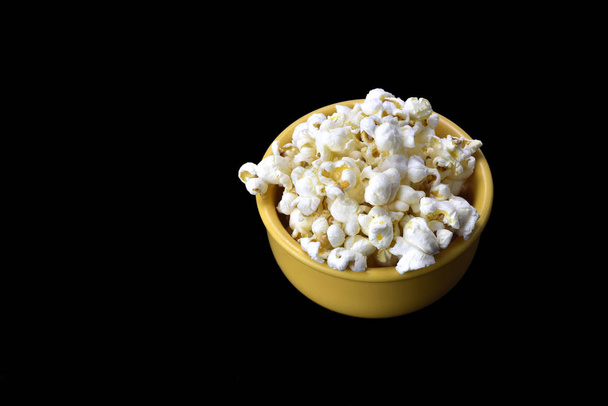 popcorn uvnitř žluté mísy na černém pozadí - Fotografie, Obrázek