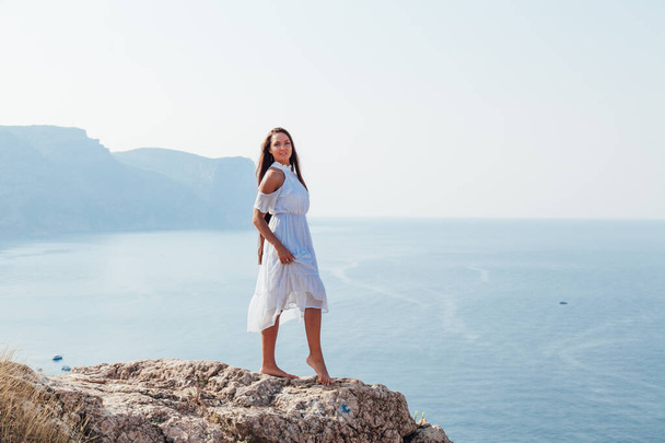 женщина с длинными волосами стоит на скале у моря - Фото, изображение