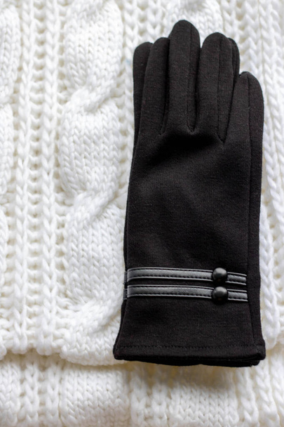 Ρούχα για μια κρύα εποχή: μάλλινο κασκόλ και γάντια. Κασκόλ λευκού χρώματος, μαύρο γάντι. Το αντικείμενο είναι απομονωμένο σε λευκό φόντο - Φωτογραφία, εικόνα