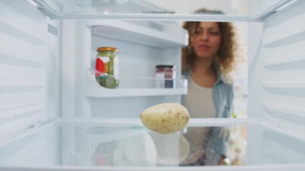 View from inside empty fridge as woman opens door and picks up potato before closing door with disappointed expression - Imágenes, Vídeo