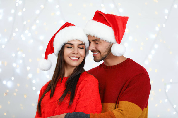 Lovely young couple in Santa hats against blurred festive lights. Christmas celebration - Foto, Imagem