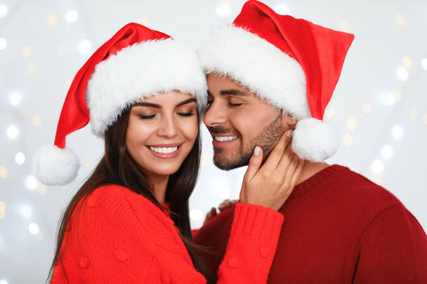 Lovely young couple in Santa hats against blurred festive lights. Christmas celebration - Foto, imagen