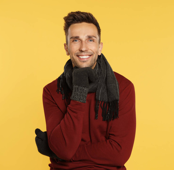 Happy young man in warm clothes on yellow background. Winter season - Φωτογραφία, εικόνα