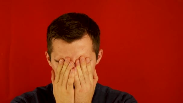 a terrified man clutches his face against a red background - Footage, Video