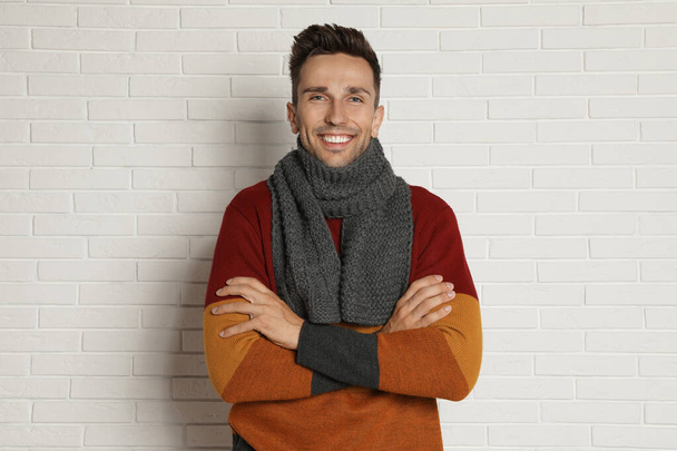 Happy young man in scarf and warm sweater near white brick wall. Winter season - 写真・画像