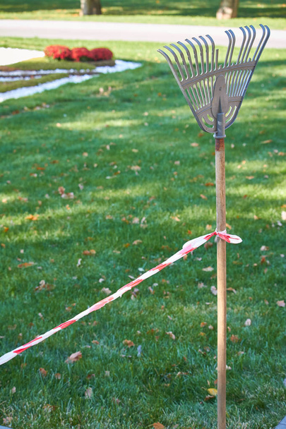 Una cinta protectora roja y blanca atada a un asa de rastrillo separa el área de limpieza en un parque público
 - Foto, imagen