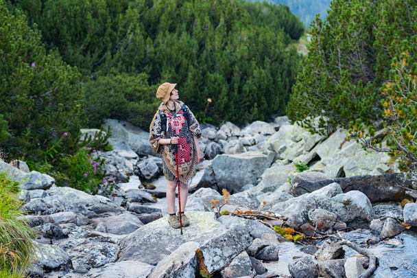 Young woman traveler in poncho and with backpack stand on the big rocks - Fotoğraf, Görsel