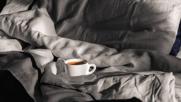 Morning coffee in bed. White cup of coffee on a gray bed in the morning sun. Enjoying the little things. Hygge. Slow life concept - Photo, Image