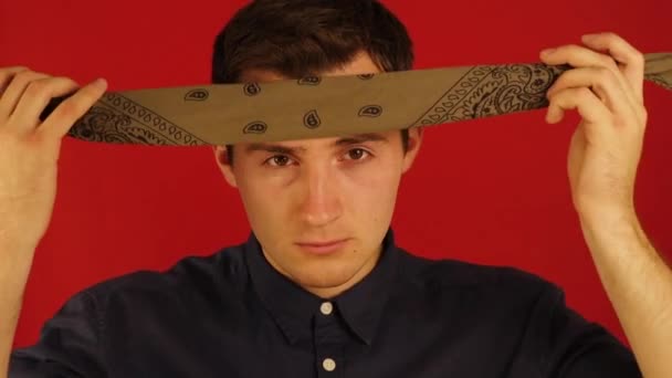 ein junger Kerl legt ein Kopftuch auf seinen Kopf auf einem isolierten roten Hintergrund - Filmmaterial, Video