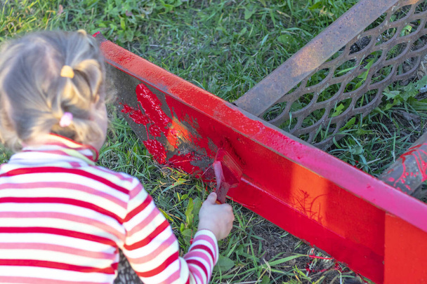 puesta de sol. Chica rubia pinta una escalera de metal con un cepillo. El color es rojo. hay un obturador. enfoque suave. teñido
 - Foto, imagen