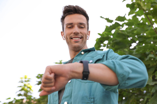 Young man with wireless earphones and smart watch in park - Photo, image
