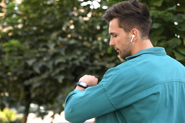Young man with wireless earphones and smart watch in park - 写真・画像