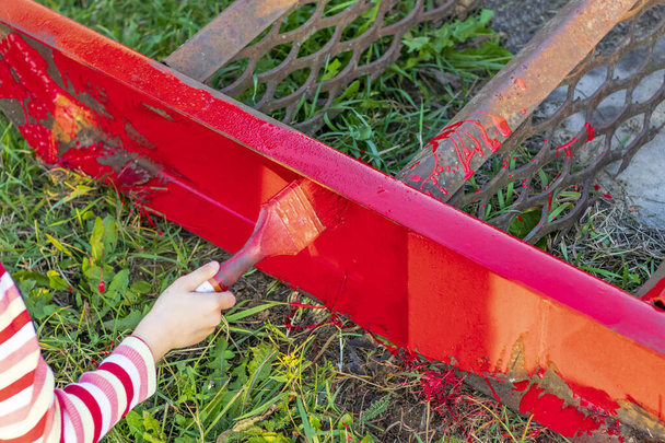 ηλιοβασίλεμα. Ξανθιά κοπέλα ζωγραφίζει μια μεταλλική σκάλα με ένα πινέλο. Το χρώμα είναι κόκκινο. Υπάρχει ένα παραθυρόφυλλο. Μαλακή εστίαση. χρωματισμός - Φωτογραφία, εικόνα