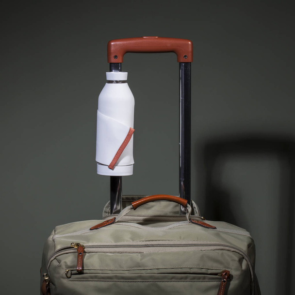 A functional drinking water bottle is attached to the handle of a travel bag and hands remain free - Photo, Image