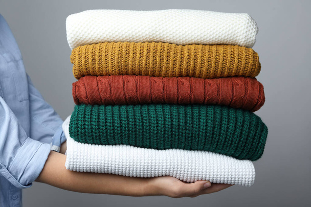 Woman holding stack of warm clothes on grey background, closeup. Autumn season - Photo, Image