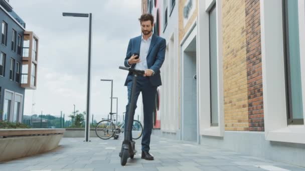 Jeune homme d'affaires vérifie son smartphone et continue à conduire pour travailler sur un scooter électrique. Un entrepreneur moderne utilise le transport écologique contemporain pour se rendre à une réunion de bureau
. - Séquence, vidéo