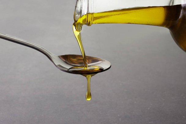 pouring olive oil from glass bottle on grey background - Фото, зображення