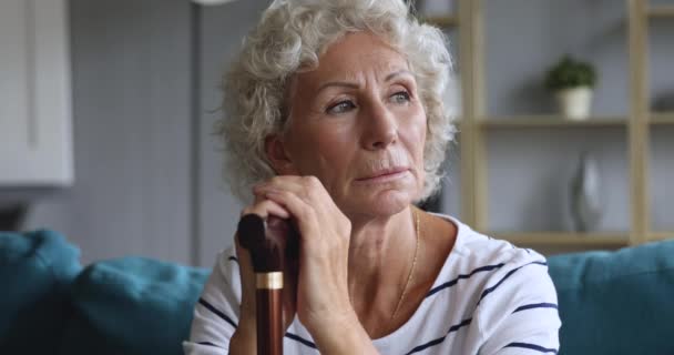 Depressed elderly woman holding walking cane stick sit on sofa - 映像、動画