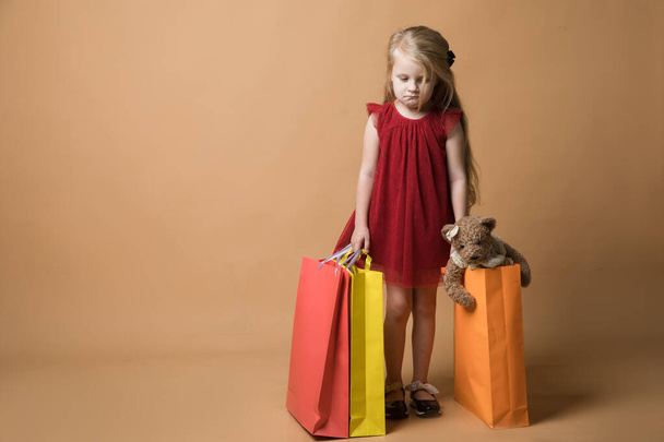 Молода дівчина в червоній сукні і з сумками, дуже щасливі покупки. Молода дівчина стоїть на помаранчевому тлі
 - Фото, зображення