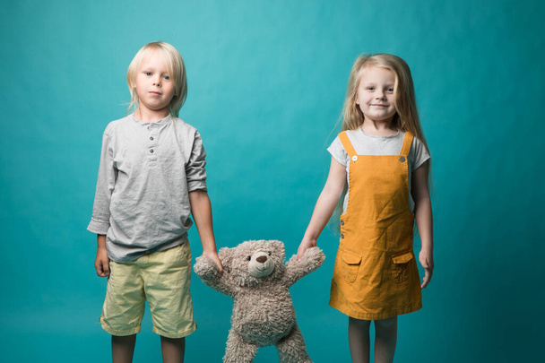 Garçon et fille sur fond bleu, tenant dans leurs mains un ours gris. Les enfants sont très joyeux. Jouets
 - Photo, image