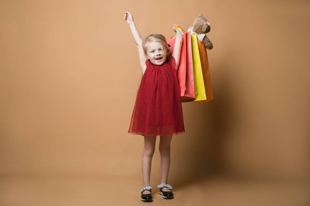 ein junges Mädchen in rotem Kleid und mit Einkaufstüten, sehr glücklich beim Einkaufen. ein junges Mädchen steht auf orangefarbenem Hintergrund - Foto, Bild