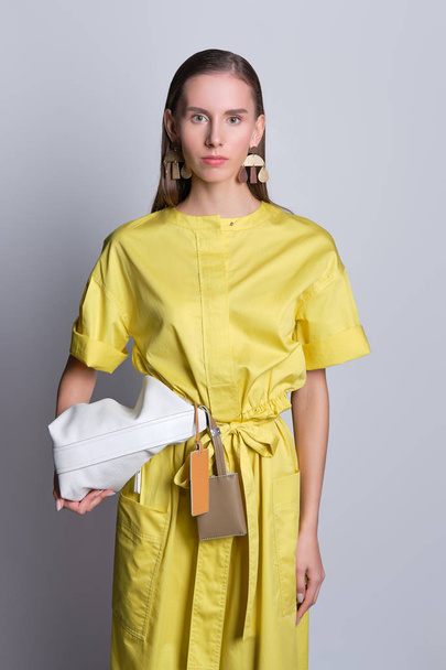 Cute fashion model in yellow dress with handbag - 写真・画像