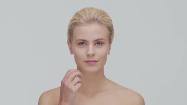 Studio portrait of young, beautiful and natural blond woman applying skin care cream. Face lifting, cosmetics and make-up. - Video