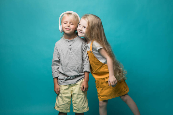 Very emotional children listen to music with headphones on a blue background. Boy and girl are dancing and showing different emotions and he is happy - Photo, Image