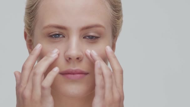 Studio portrait of young, beautiful and natural blond woman applying skin care cream. Face lifting, cosmetics and make-up. - Filmagem, Vídeo