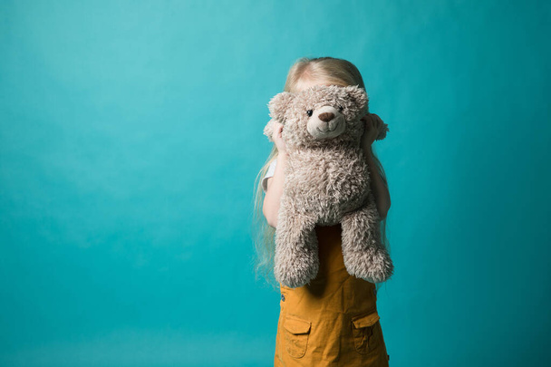 Girl on a blue background hugging a gray bear. She is very happy - Фото, изображение