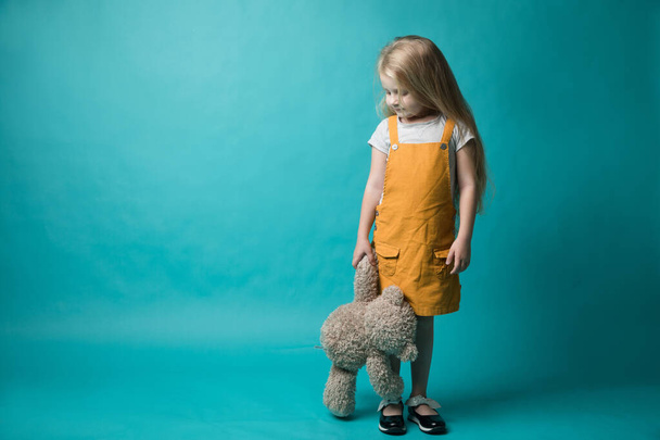 girl on a blue background, holding in hands a grey bear. Toys - Foto, Imagem