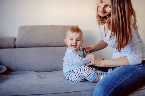 Adorable smiling baby boy 6 months old learning how to sit. His mother holding his hands and teaching him. - Φωτογραφία, εικόνα