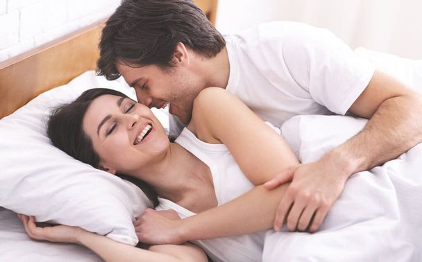 Νεαρός φιλάει την κοπέλα του στο κρεβάτι - Φωτογραφία, εικόνα