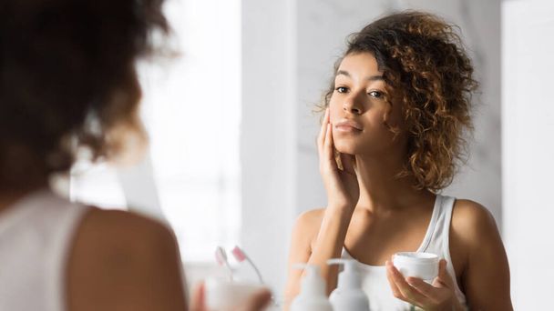 Csinos fekete lány alkalmazása arckrém álló fürdőszoba, panoráma - Fotó, kép