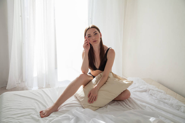 beautiful woman in laundry in the morning sits on the bed with a pillow - Photo, Image