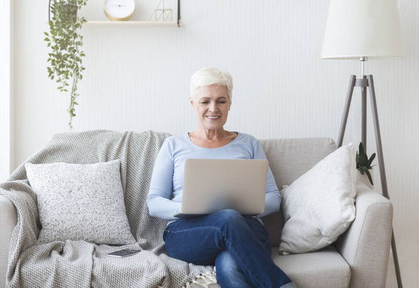 Ambitious senior lady using laptop on sofa at home - Photo, Image