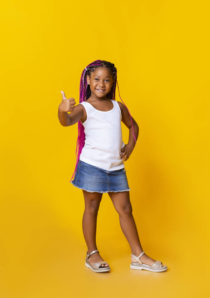 Adorável afro menina gestos polegares para cima no estúdio amarelo fundo
 - Foto, Imagem