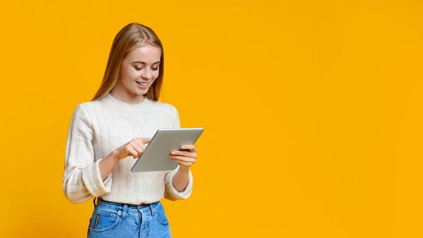 Beautiful teen girl using digital tablet over orange studio background - Фото, изображение
