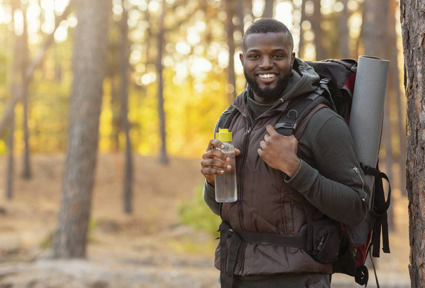 African man wearing backpack standing over forest background - 写真・画像