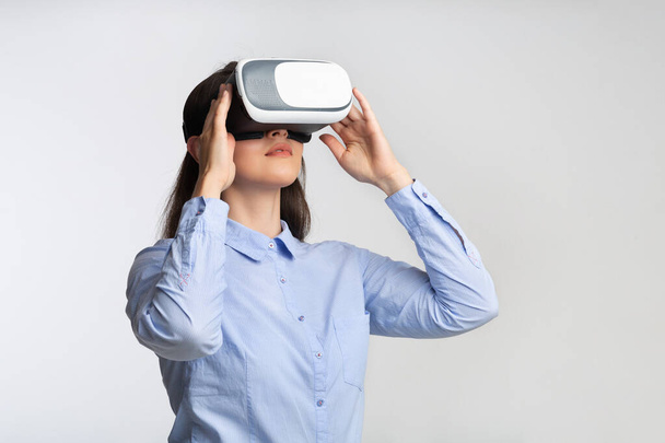Fiatal nő virtuális valóság headset álló felett szürke háttér - Fotó, kép